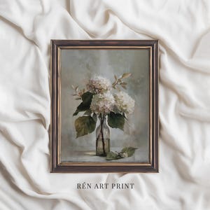 May include: A framed art print featuring a still life of white hydrangeas in a clear glass bottle. The painting has a soft, muted color palette with green leaves and a brown frame. The text "R&Eacute;N ART PRINT" is at the bottom.