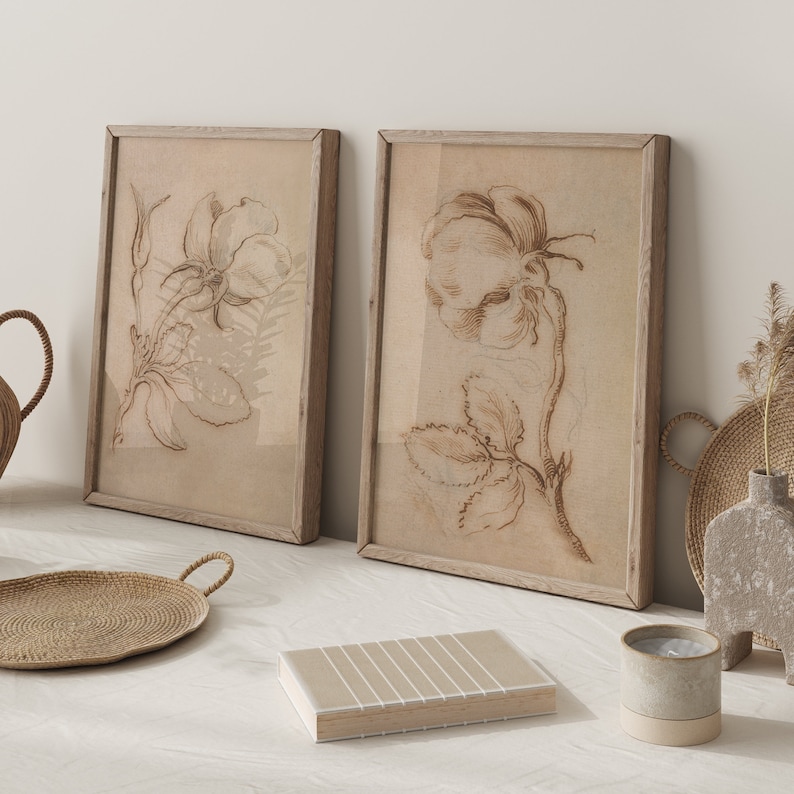 May include: Two framed botanical prints with detailed line drawings of roses in a light brown color scheme. The frames are a light wood color.