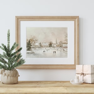 May include: A framed watercolour painting depicting a winter scene with people ice skating on a frozen lake in front of a small town. The painting has a soft, muted colour palette with shades of brown, grey, and white.