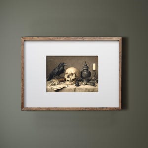May include: A framed print featuring a still life with a raven, skull, antique lamp, and candle. The artwork has a vintage aesthetic with sepia tones. The raven is perched near the skull, creating a gothic or Halloween theme.