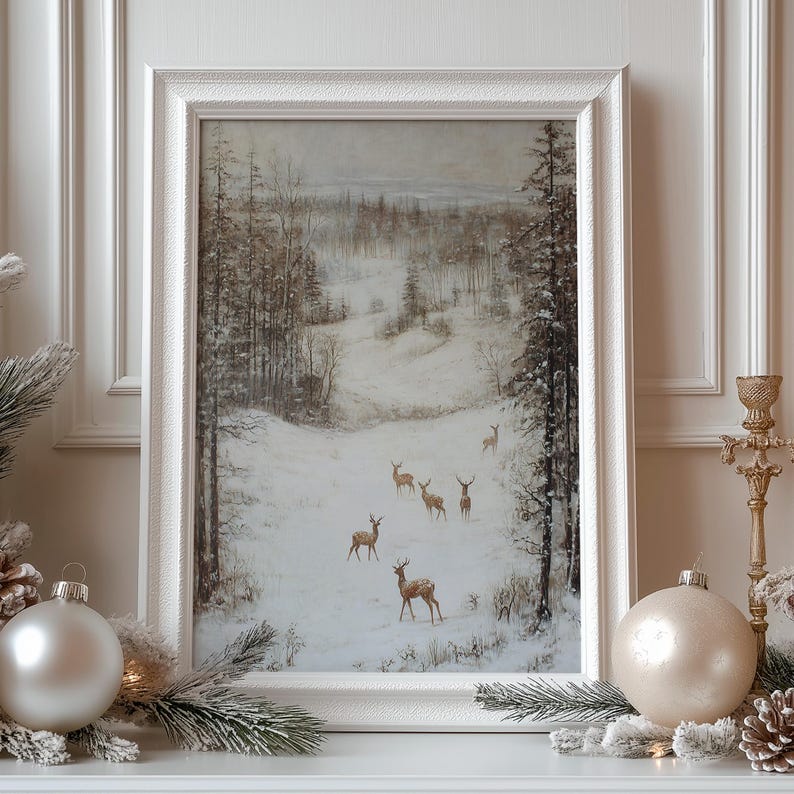 Op de afbeelding: Een ingelijste winterlandschapsschilderij met een besneeuwde bossc&egrave;ne met verschillende herten. Het kunstwerk staat in een witte lijst en is versierd met kerstversieringen en dennentakken.