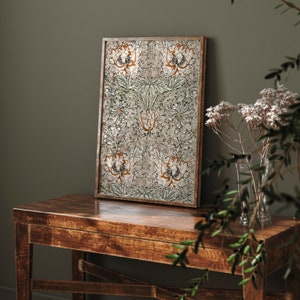 May include: A framed print with a floral pattern in shades of green, white, and orange. The print is hanging on a wall above a wooden table.