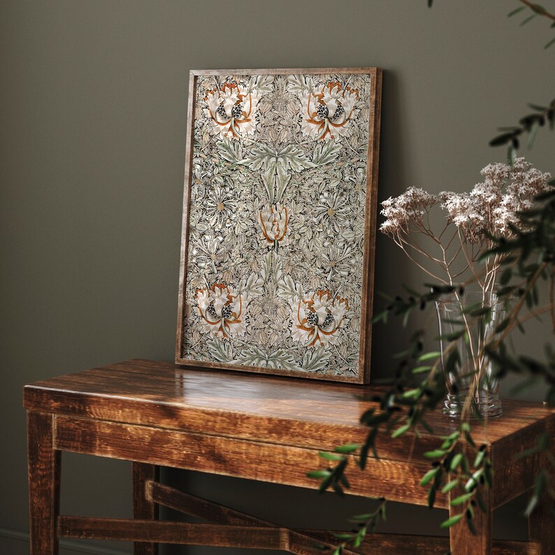 May include: A framed print with a floral pattern in shades of green, white, and orange. The print is hanging on a wall above a wooden table.