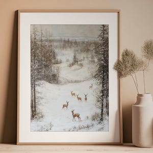 Op de afbeelding: Ingelijste kunstdruk met een winterlandschap met herten. Het kunstwerk toont een besneeuwd veld omgeven door bomen, met verschillende herten. Het kleurenpalet is gedempt, met tinten bruin, wit en grijs. De print zit in een licht houten frame.