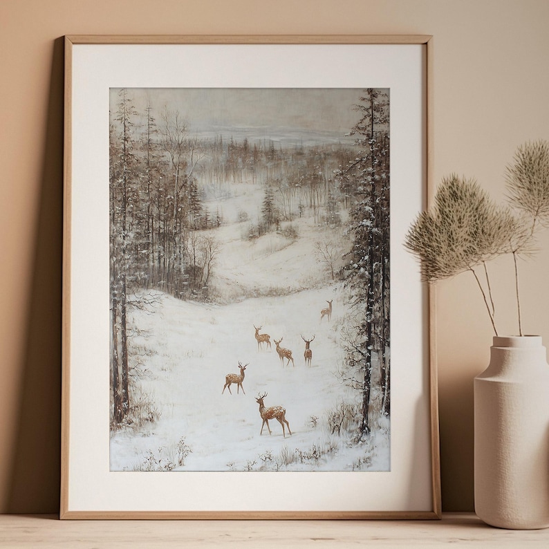 Op de afbeelding: Ingelijste kunstdruk met een winterlandschap met herten. Het kunstwerk toont een besneeuwd veld omgeven door bomen, met verschillende herten. Het kleurenpalet is gedempt, met tinten bruin, wit en grijs. De print zit in een licht houten frame.
