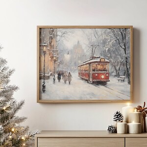 May include: A framed winter landscape painting depicts a red trolley car on a snow-covered street. People walk along the sidewalk, and the scene is illuminated by streetlights. The artwork is in a wooden frame.