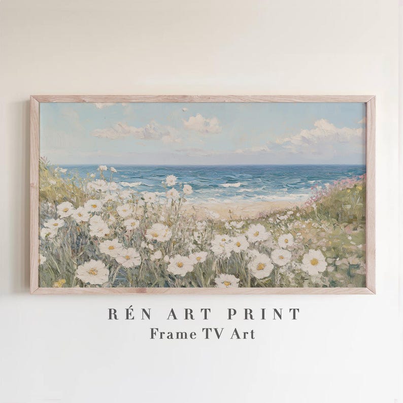 May include: A framed landscape painting of a beach scene. White flowers bloom in the foreground, with a sandy beach, blue ocean, and sky with clouds in the background. The text "R&Eacute;N ART PRINT Frame TV Art" is at the bottom.
