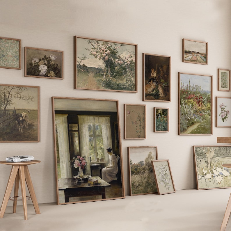 Op de afbeelding: Een galeriewand met een verscheidenheid aan ingelijste kunstwerken, waaronder landschappen, stillevens en portretten. De kunstwerken zijn symmetrisch gerangschikt op een witte muur.