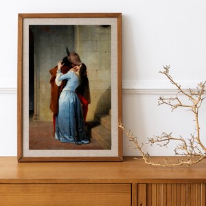 May include: A painting of a couple kissing in a hallway. The man is wearing a brown coat and a hat, and the woman is wearing a blue dress. The painting is set against a backdrop of stone walls and a staircase.