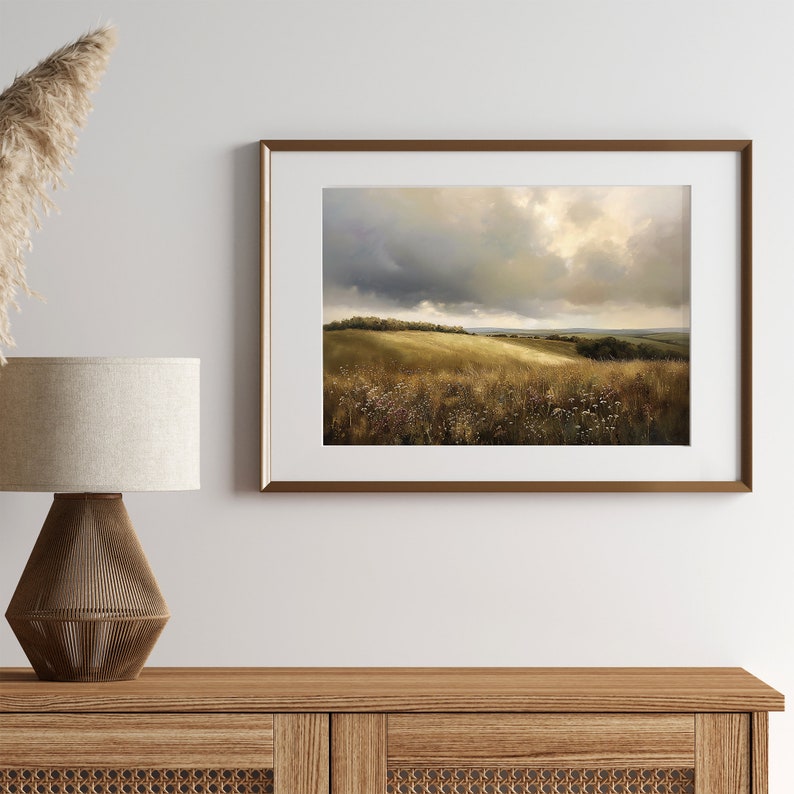 Peut inclure: Une peinture de paysage encadr&eacute;e repr&eacute;sentant un champ de gazon dor&eacute; ondulant sous un ciel nuageux. La peinture est dans un cadre dor&eacute; et est accroch&eacute;e &agrave; un mur blanc.