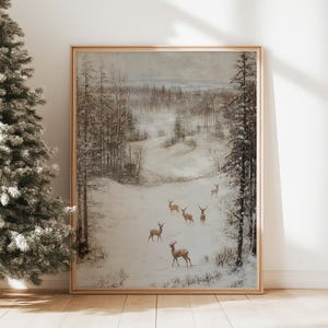 Op de afbeelding: Een ingelijst winterlandschapsschilderij met een kudde herten in een besneeuwd bos. Het kunstwerk heeft een gedempt kleurenpalet met tinten bruin, grijs en wit. Het schilderij zit in een houten lijst.