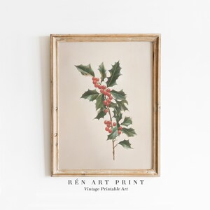 以下が含まれることがあります： 緑の葉と赤い実が付いたヒイラギの枝の植物画が描かれた、額入りのヴィンテージアートプリント。プリントはベージュの背景で、金色の木製フレームに入っています。「RÉN ART PRINT Vintage Printable Art」の文字が下部にあります。
