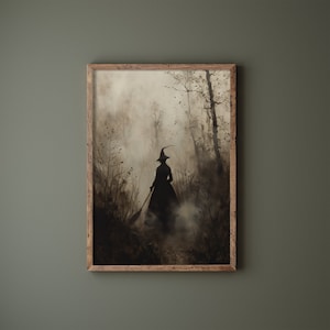 May include: A framed print showing a silhouetted witch in a forest, holding a broom. The artwork uses black, grey, and brown tones, creating a misty, atmospheric effect. The wooden frame provides a rustic element to the spooky scene.