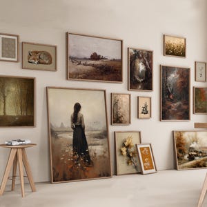 May include: A gallery wall arrangement featuring multiple framed art prints in various sizes. The collection includes landscapes, a sleeping fox, a person standing in a field, a steam train, and botanical illustrations in muted earth tones.
