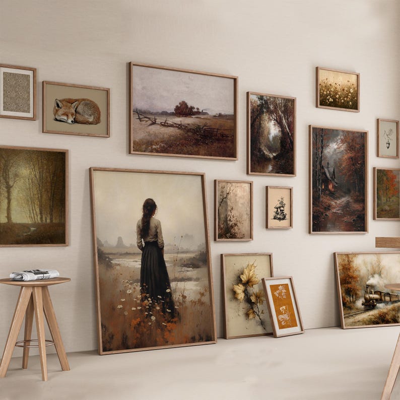 May include: A gallery wall arrangement featuring multiple framed art prints in various sizes. The collection includes landscapes, a sleeping fox, a person standing in a field, a steam train, and botanical illustrations in muted earth tones.