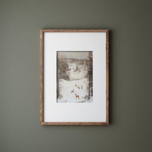 Op de afbeelding: Ingelijst kunstwerk met een winterlandschap met herten in een besneeuwde sc&egrave;ne. Het schilderij is gevat in een rustieke houten lijst met een witte passe-partout. Het kunstwerk toont een bos en een met sneeuw bedekt veld.