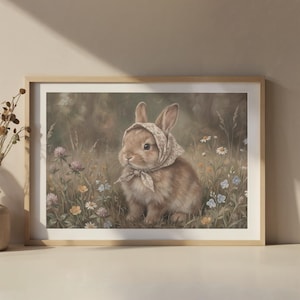 May include: A framed print featuring a brown rabbit wearing a headscarf, sitting in a field of wildflowers. The artwork has a soft, painterly style with a natural color palette, including greens, blues, and pinks. The rabbit is the focal point.