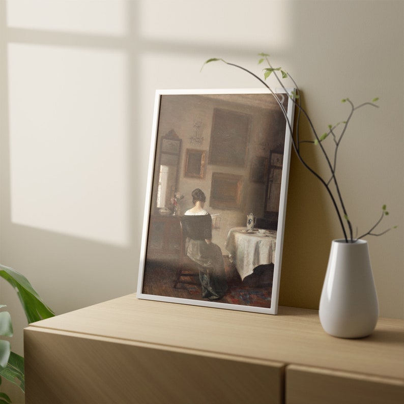May include: A framed painting of a woman sitting in a chair in a room with a table and chairs. The woman is wearing a dark dress and is looking down at something in her lap. The room is decorated with a few pieces of furniture and a few paintings on the walls.