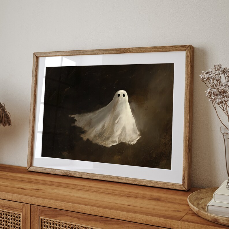 Puede incluir: Una impresi&oacute;n art&iacute;stica enmarcada que presenta un fantasma blanco con ojos negros sobre un fondo oscuro. El fantasma parece estar flotando. La obra de arte se muestra en un marco de madera, a&ntilde;adiendo un toque r&uacute;stico a la escena espeluznante.