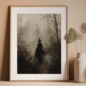 May include: Framed art print depicting a witch silhouette in a long dress and pointed hat, walking through a misty forest. The artwork is in shades of grey and brown, with a vintage, gothic aesthetic. The witch is holding a broom.
