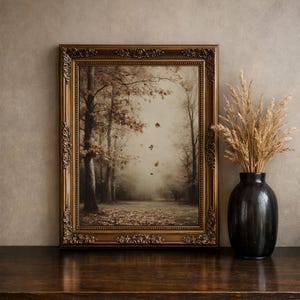 May include: A rectangular wall art piece in an ornate, antique bronze-colored frame featuring a sepia-toned forest scene with falling autumn leaves. Beside the frame sits a black ceramic vase filled with dried, light brown ornamental grasses.