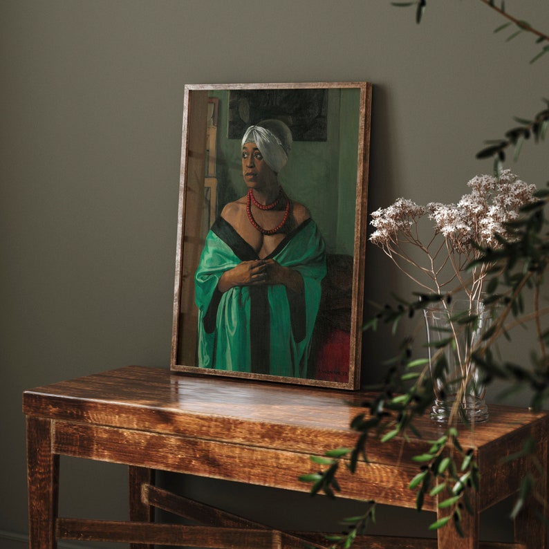 Puede incluir: Un retrato enmarcado de una mujer con un pa&ntilde;uelo blanco en la cabeza, un collar de cuentas rojas y una t&uacute;nica verde con ribetes negros. La pintura se exhibe sobre una mesa de madera, con un jarr&oacute;n de flores secas en el fondo.