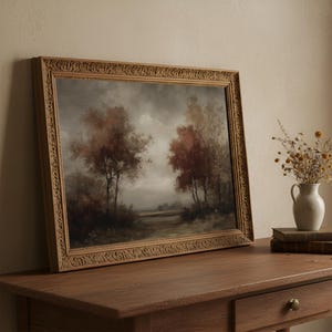 May include: A landscape painting in an ornate, carved wooden frame depicting trees with autumn-colored foliage under a cloudy, overcast sky. The artwork features muted tones of brown, rust, and grey, capturing a quiet, natural scene.