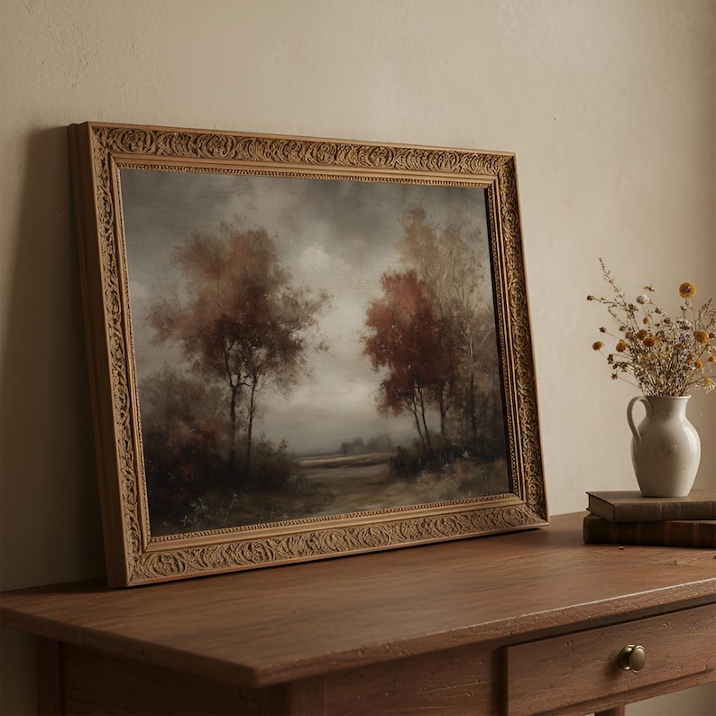 May include: A landscape painting in an ornate, carved wooden frame depicting trees with autumn-colored foliage under a cloudy, overcast sky. The artwork features muted tones of brown, rust, and grey, capturing a quiet, natural scene.