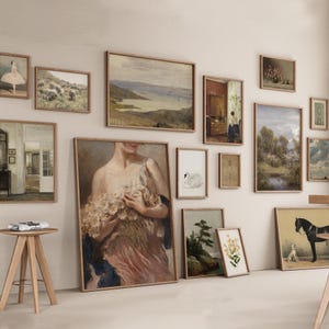 May include: A gallery wall featuring a selection of framed artwork, including landscapes, portraits, and still lifes. The artwork is arranged in a symmetrical pattern on a white wall.