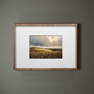 Peut inclure: Une peinture de paysage encadr&eacute;e repr&eacute;sentant un champ avec des collines vallonn&eacute;es et un ciel nuageux. La peinture est dans un cadre en bois avec un passe-partout blanc.