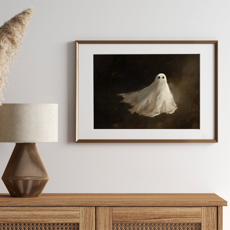 Puede incluir: Una impresi&oacute;n enmarcada que presenta un fantasma blanco con ojos negros sobre un fondo oscuro. El fantasma parece estar flotando, con su forma de s&aacute;bana ondeando. La obra de arte est&aacute; enmarcada en un marco dorado, agregando un toque de elegancia.