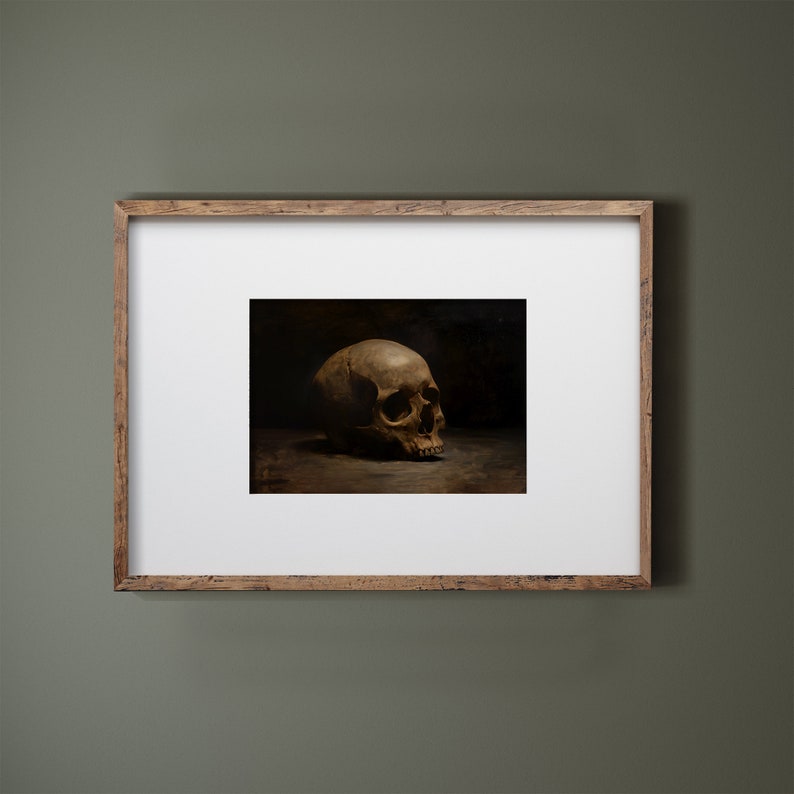 May include: A framed print of a still life featuring a human skull in a dark setting. The skull is positioned on a dark surface and is lit from the left side, casting shadows.