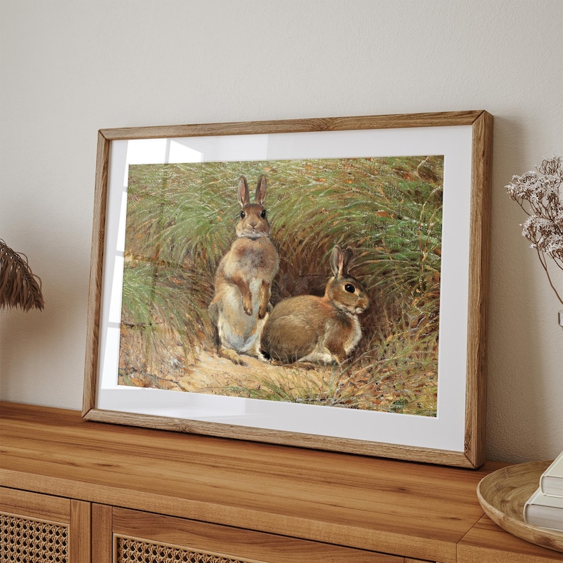 May include: A framed painting of two brown rabbits in a grassy field. The rabbits are standing upright and looking at the viewer. The painting is set against a white background.