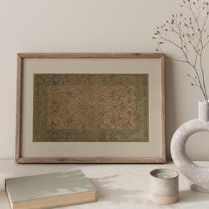 May include: A rectangular framed print featuring a vintage-style rug pattern with a central tan field, intricate floral motifs in muted blue and green, and a wide decorative border, all encased in a light-toned wooden frame with a beige mat.