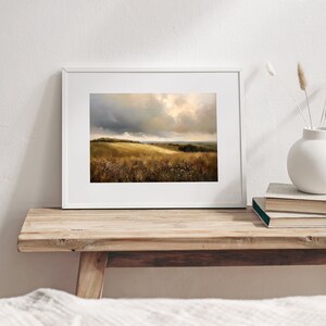 Peut inclure: Une peinture de paysage encadr&eacute;e repr&eacute;sentant un champ d'herbe dor&eacute;e sous un ciel nuageux. La peinture est dans un cadre blanc et est pos&eacute;e sur une &eacute;tag&egrave;re en bois.