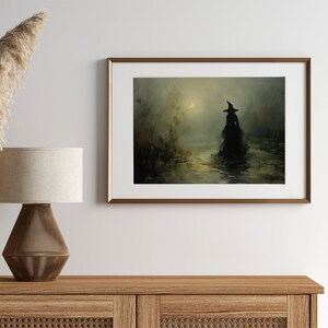 May include: Framed artwork depicting a silhouetted figure in a witch's hat and gown wading through water. The painting has a dark, moody color palette with a hazy, atmospheric quality. The artwork is displayed in a gold-toned frame, adding a touch of elegance.