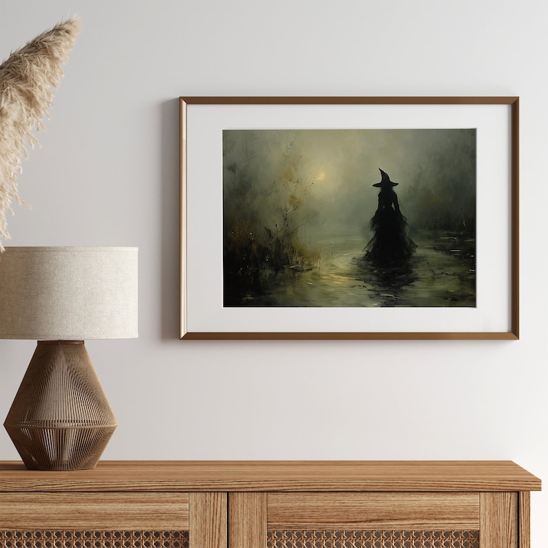 May include: Framed artwork depicting a silhouetted figure in a witch's hat and gown wading through water. The painting has a dark, moody color palette with a hazy, atmospheric quality. The artwork is displayed in a gold-toned frame, adding a touch of elegance.