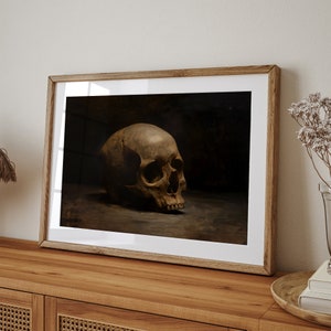 May include: A framed print of a still life featuring a human skull in a dark setting. The skull is positioned on a surface and is the focal point of the image.