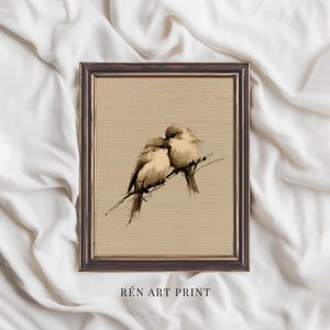 May include: A framed art print featuring a sepia-toned illustration of two birds perched on a branch. The birds are depicted in a soft, painterly style, with delicate brushstrokes. The frame is dark brown, and the text "RÉN ART PRINT" is at the bottom.