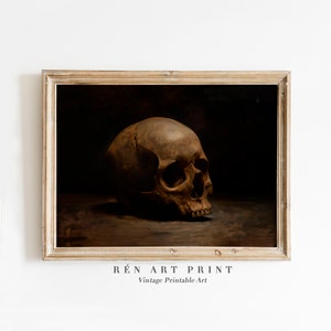 May include: A vintage art print of a human skull in a dark brown frame. The skull is painted in a realistic style and is positioned on a dark brown surface. The print is titled "R&Eacute;N ART PRINT" and "Vintage Printable Art".