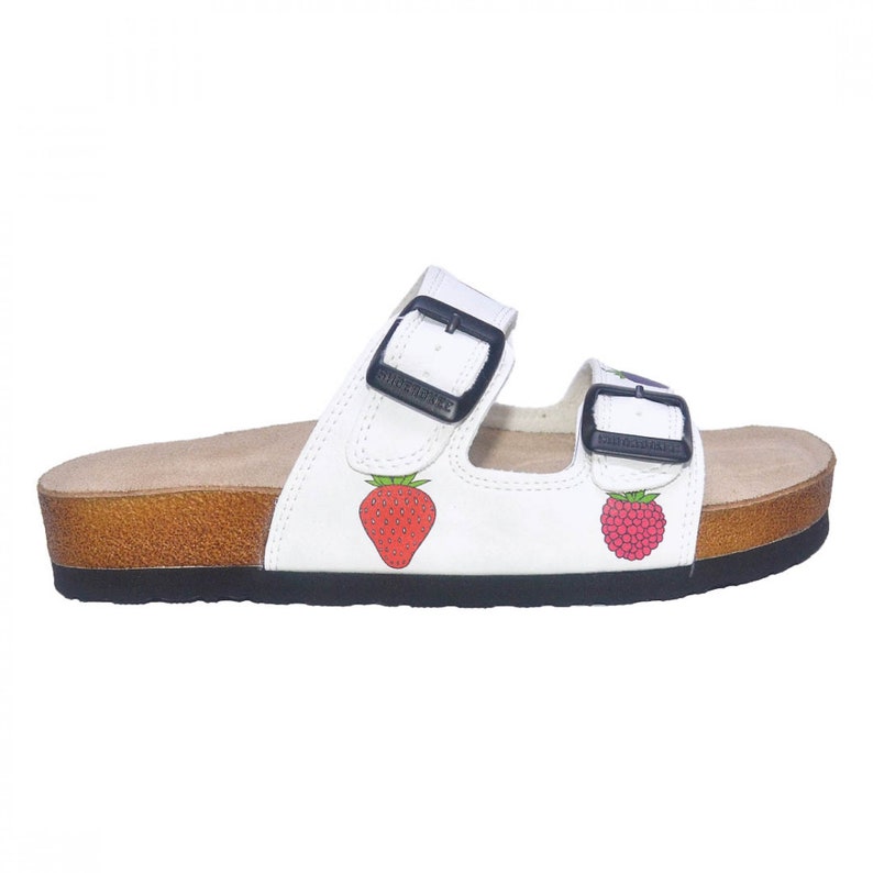 May include: White leather sandals with two adjustable buckles. The sandals have a cork platform and feature a strawberry and raspberry design.