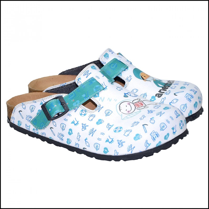 May include: White clogs with a blue and green pattern. The clogs have a buckle strap and a cork footbed. The pattern includes a variety of small icons and a cartoon character.