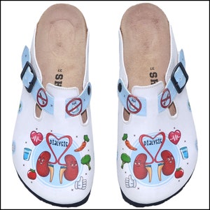 Könnte beinhalten: Weiße Clogs mit einem blau-weißen Design mit Comic-Nieren, einem Herzen, einem Glas Wasser und dem Wort "Dialyse".