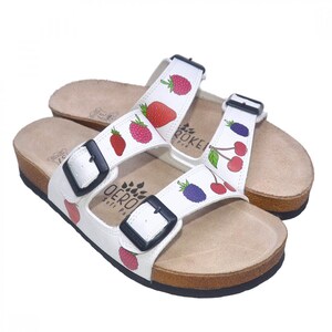 May include: White leather sandals with adjustable buckles and a cork sole. The sandals feature a colorful fruit print with strawberries, raspberries, cherries, and blackberries.