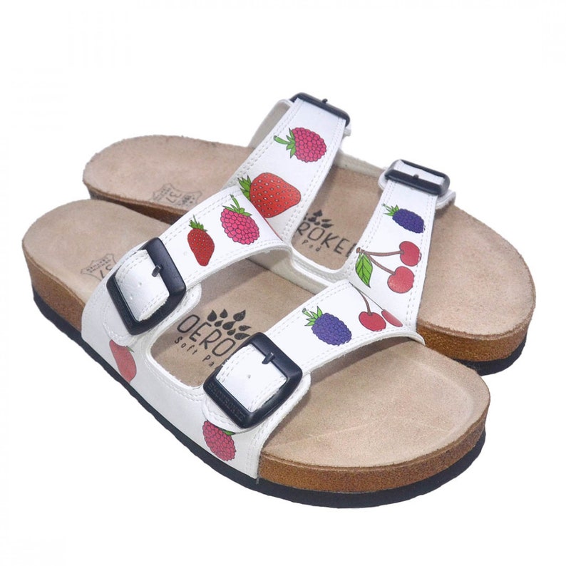 May include: White leather sandals with adjustable buckles and a cork sole. The sandals feature a colorful fruit print with strawberries, raspberries, cherries, and blackberries.