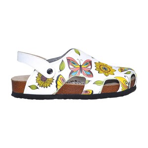 K&ouml;nnte beinhalten: Wei&szlig;e Ledersandalen mit Schmetterlings- und Sonnenblumenmuster. Die Sandalen haben ein Korkfu&szlig;bett und eine schwarze Gummisohle.