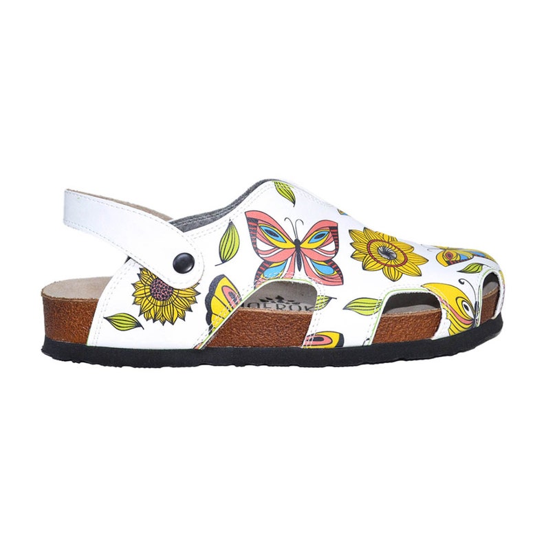 K&ouml;nnte beinhalten: Wei&szlig;e Ledersandalen mit Schmetterlings- und Sonnenblumenmuster. Die Sandalen haben ein Korkfu&szlig;bett und eine schwarze Gummisohle.