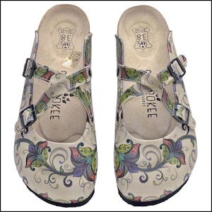 May include: Pair of beige leather clogs with a colorful floral pattern. The clogs have adjustable buckles and the word "OKEE" printed on the side. The size is 38.