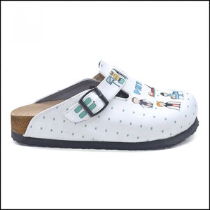 May include: White leather clog with a green and blue patterned design. The clog has a cork sole and a black buckle. The design features a family of stick figures with the text "Pati" on the shoe.