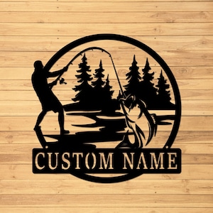 May include: Black metal silhouette of a person fishing in a lake with trees in the background. The silhouette is inside a circle with the text "CUSTOM NAME" below it.